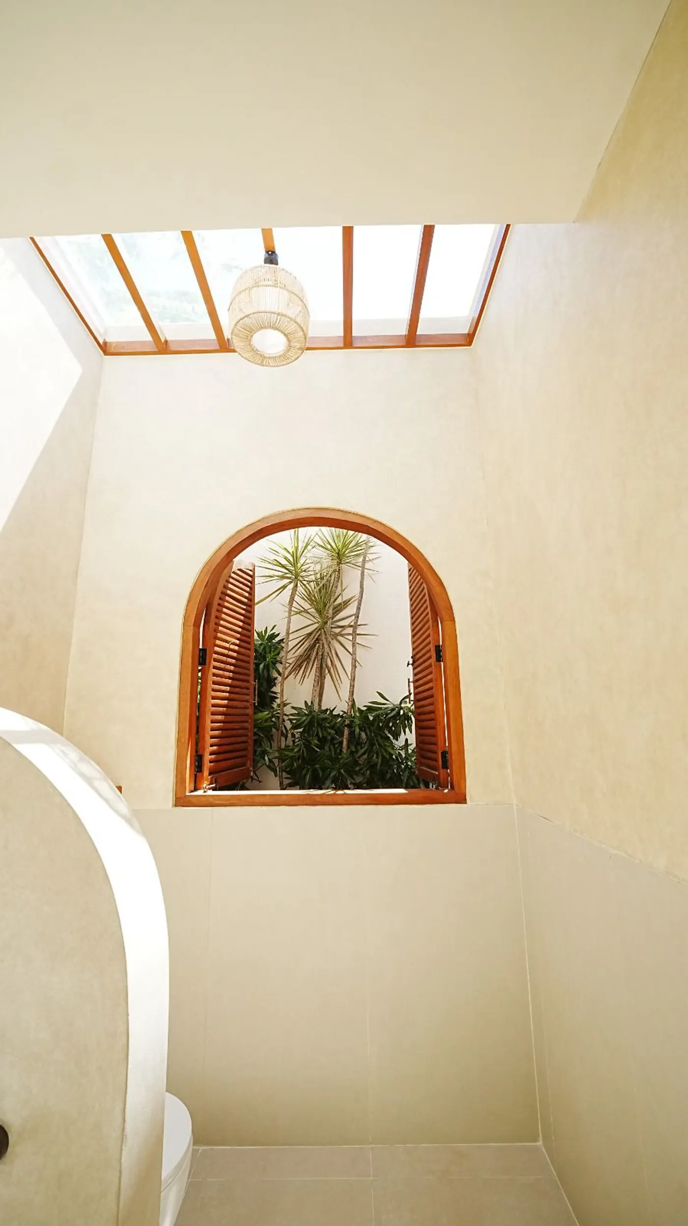 An arched window set into a cream plaster wall beneath a timber skylight