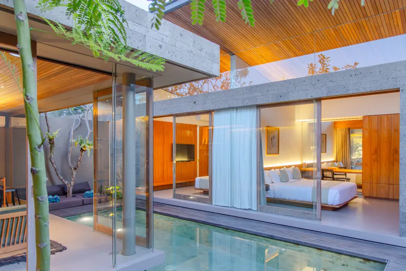 Glass pavilion bedroom over a pool beneath a timber ceiling in a Bali villa