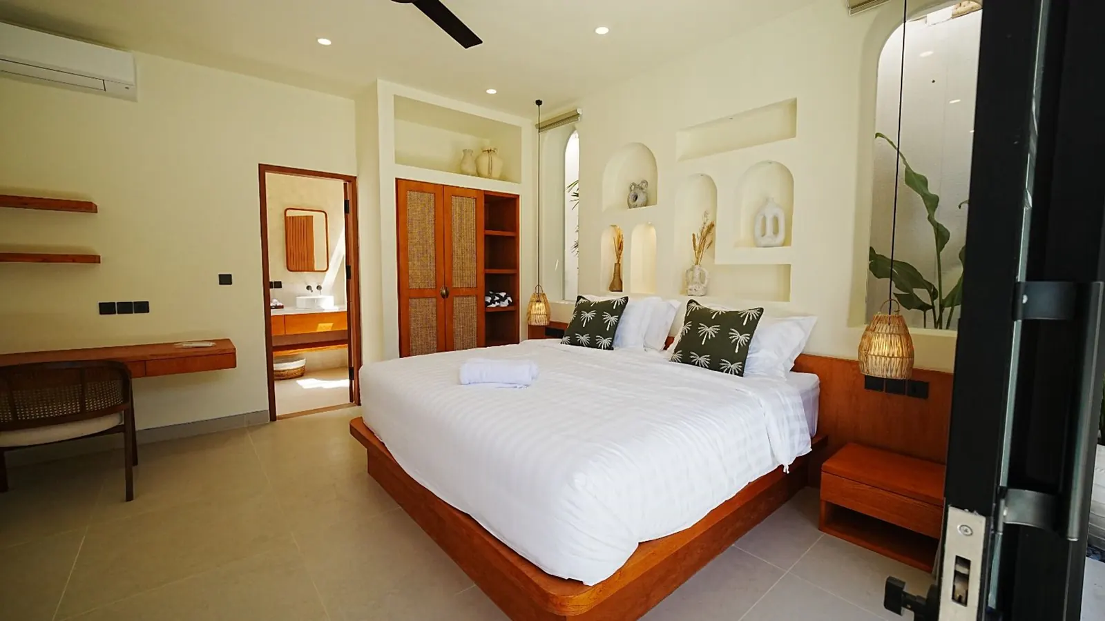 A bedroom with teak furniture, arched niches and white linen